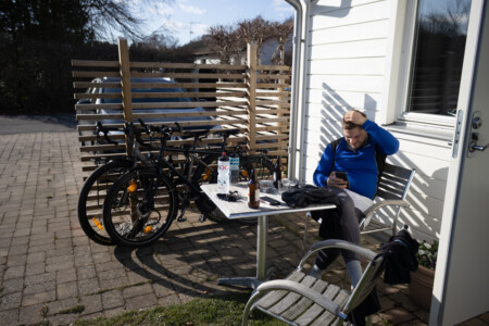 A man sitting in the sun with two bikes and some beer.